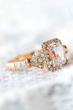 a gold ring with an emerald stone surrounded by white diamonds, on top of a marble surface