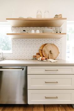 a white kitchen with open shelving and stainless steel dishwasher