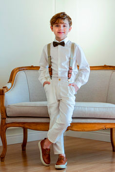 a young boy dressed in white with suspenders and a bow tie