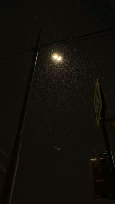 the street light is lit up in the dark night sky with snow falling on it