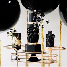 a black and gold cake with balloons in the background