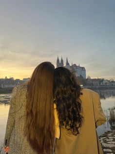 two women standing next to each other looking at the water and buildings in the background