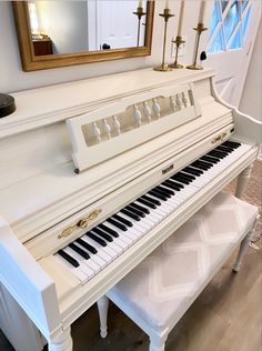 a white piano sitting on top of a hard wood floor next to a mirror and bench