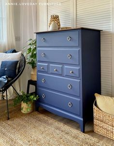 a blue dresser sitting in front of a window next to a wicker basket and chair