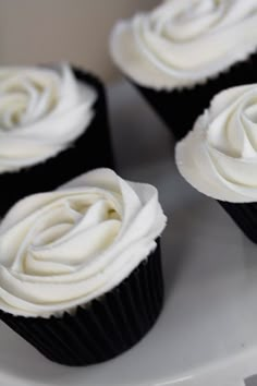 four cupcakes with white frosting sitting on a plate