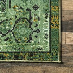 a green rug with an ornate design on top of wooden flooring and wood planks