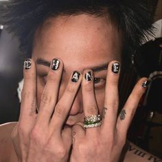 a man with black and white nail polish holding his hands to his face