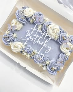 a birthday cake with blue frosting and white flowers in a box on a table