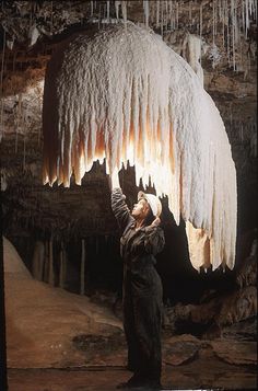 a man standing in front of a large icicles hanging from the side of a cave