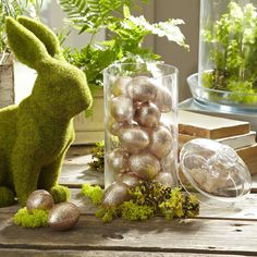 an easter bunny sitting on top of a wooden table next to some plants and eggs