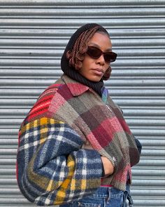 a woman wearing sunglasses and a plaid coat is standing in front of a garage door