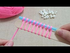 someone is knitting with pink yarn and white beads on the table next to some crochet hooks