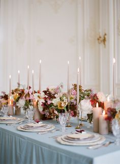 the table is set with candles, plates and vases filled with flowers on it