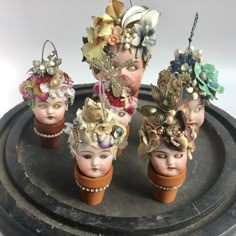 four small head vases with flowers and pearls on them sitting on a black tray