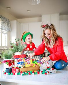 a woman and her child are sitting on the kitchen counter with christmas gifts in front of them