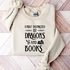 Easily Distracted By Dragons And Books Sweatshirt | Fantasy Book Lover Shirt | Reading Sweater | Book Crewneck | Dragon Book Sweatshirt Thank you for considering purchasing from Raven Printing Company.  We are based out of Cleveland, Ohio and would love to have the opportunity to earn your business. Because we are a small business, we cannot accept returns or exchanges.  However, if your product does not meet your standards please reach out and we would be more than happy to work with you on a s Bookish Cotton Sweatshirt With Letter Print, White Bookish Sweatshirt With Letter Print, Cotton Letter Print Bookish Sweatshirt, Literary Long Sleeve Cotton Tops, Literary White Cotton Tops, White Cotton Literary Tops, Sweatshirt And Shirt Outfit, Book Crewneck, Dragon Book