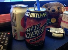 a teddy bear sitting next to a can of soda and a remote control on a desk