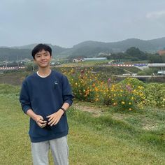 a young man standing on top of a lush green field next to flowers and mountains