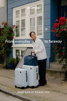 a woman holding two suitcases on the sidewalk in front of a blue and white house