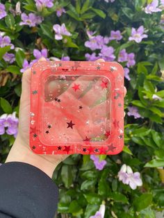 someone holding up a plastic container with stars on it in front of some purple flowers