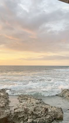 an umbrella sitting on top of a rocky beach next to the ocean at sunset or dawn