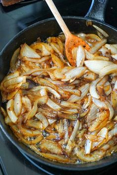 onions being cooked in a skillet with a wooden spoon