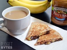 a cup of coffee next to some food on a napkin with bananas and peanut butter in the background