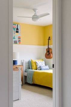 a bedroom with yellow walls and a guitar hanging on the wall next to the bed