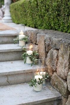 candles are lined up on the steps with greenery in glass vases next to them