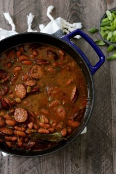 a pot filled with beans and sausage on top of a wooden table next to other vegetables