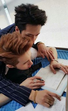 two people sitting at a table with books and papers in front of them, looking at each other