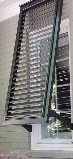 an open window on the side of a white brick building with blinds pulled up to it's sides