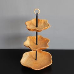 three tiered wooden tray with black handles on a dark countertop, in front of a gray wall