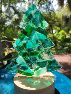 a green glass christmas tree sitting on top of a blue table in front of trees