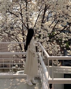 a woman standing on a balcony next to a tree with white flowers in the background