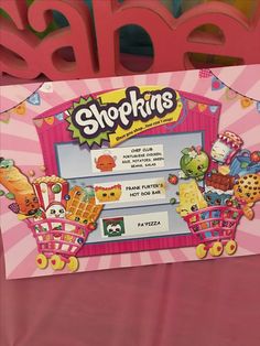 a pink shopping bag with shopkins's on the front and back sides, sitting next to a sign that says shopkinss