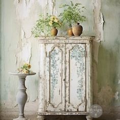 an old cabinet with flowers and vases on it in front of a peeling wall