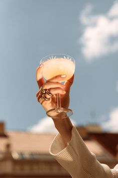 a woman holding up a wine glass in front of a building with a sky background