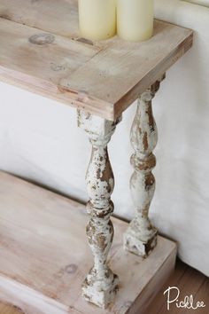 two candles sitting on top of a wooden table next to a white wall and wood floor