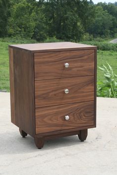 a brown wooden cabinet sitting on top of a cement floor in front of some trees