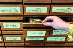 a person's hand is reaching for some food in a wooden drawer with labels on it