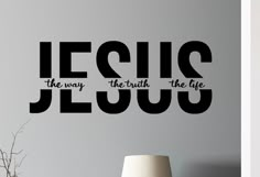 the word jesus is written in black on a wall next to a vase and lamp