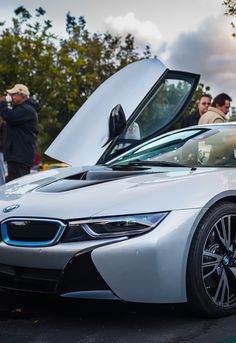 a white bmw sports car with its hood open and people standing around looking at it