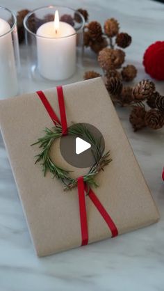 a present wrapped in brown paper with a red ribbon and pine cones around it on a table