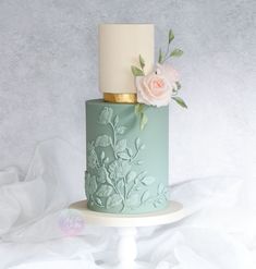 a green and white cake with flowers on top is sitting on a stand against a gray background