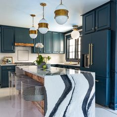 a kitchen with blue cabinets and marble counter tops in the center, along with two pendant lights