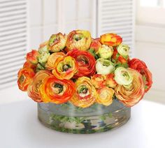 an arrangement of orange and yellow flowers in a glass vase on a white table top