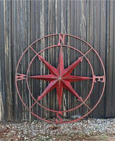 a red metal compass sitting next to a wooden fence