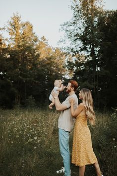 a man and woman holding a baby in their hands while standing in the middle of a field