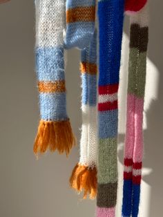 two scarves hanging from a hook on a white wall, one with multicolored stripes and the other with tassels